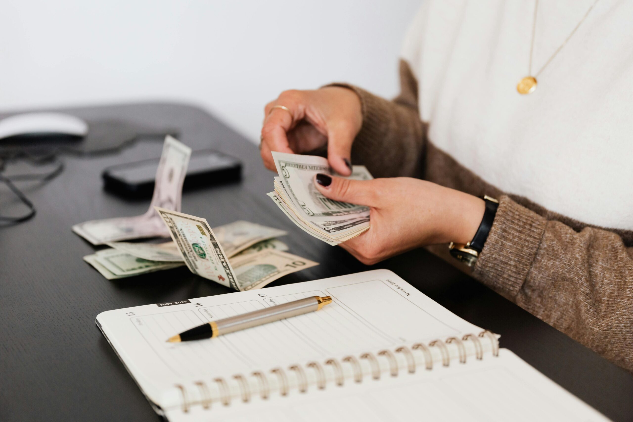 Woman counting money with a notebook and pen aiming to Stop Emotional Spending