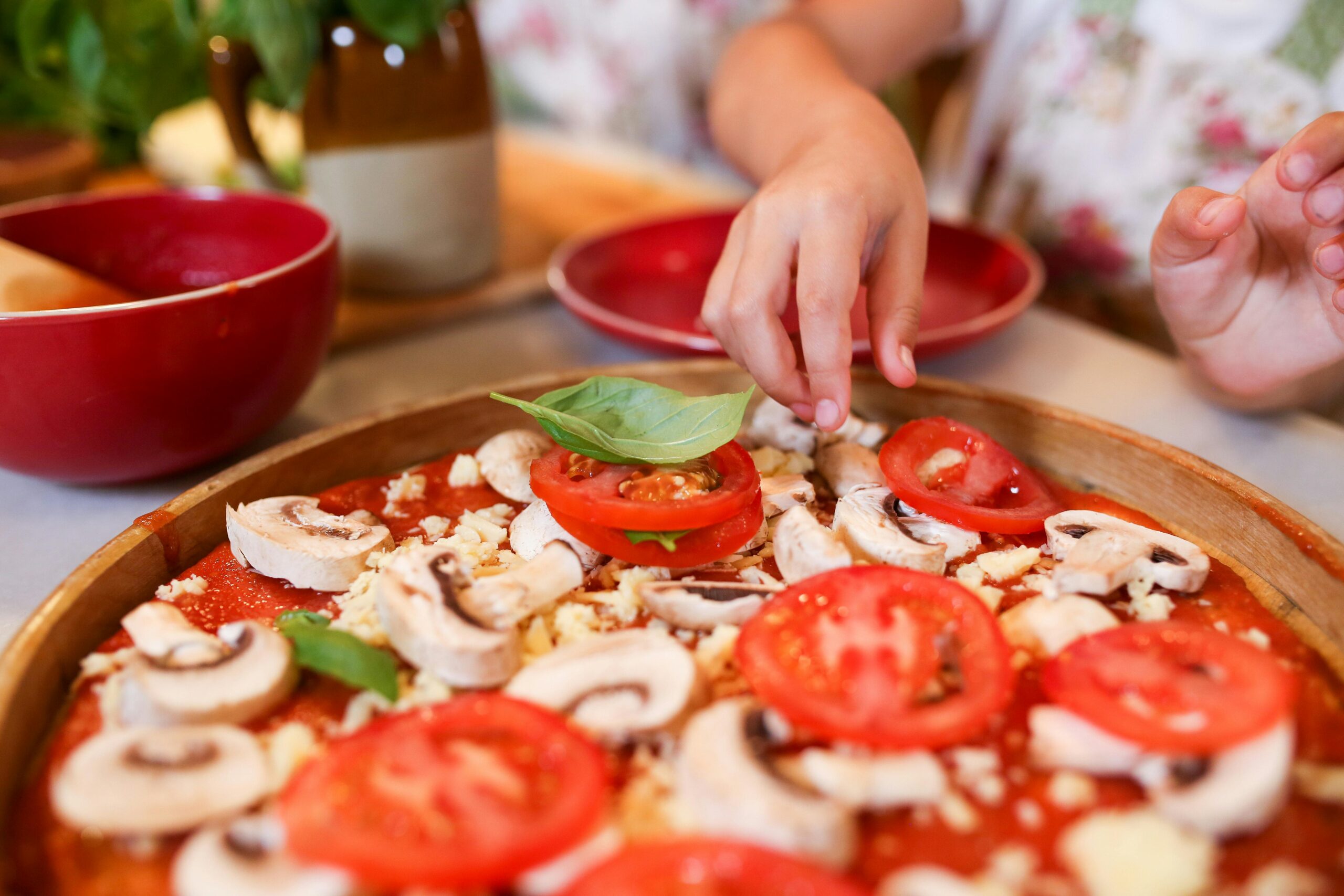 a hand adding tomatoe and basil to a pizza one of my recipes for weekly meal plan for busy moms